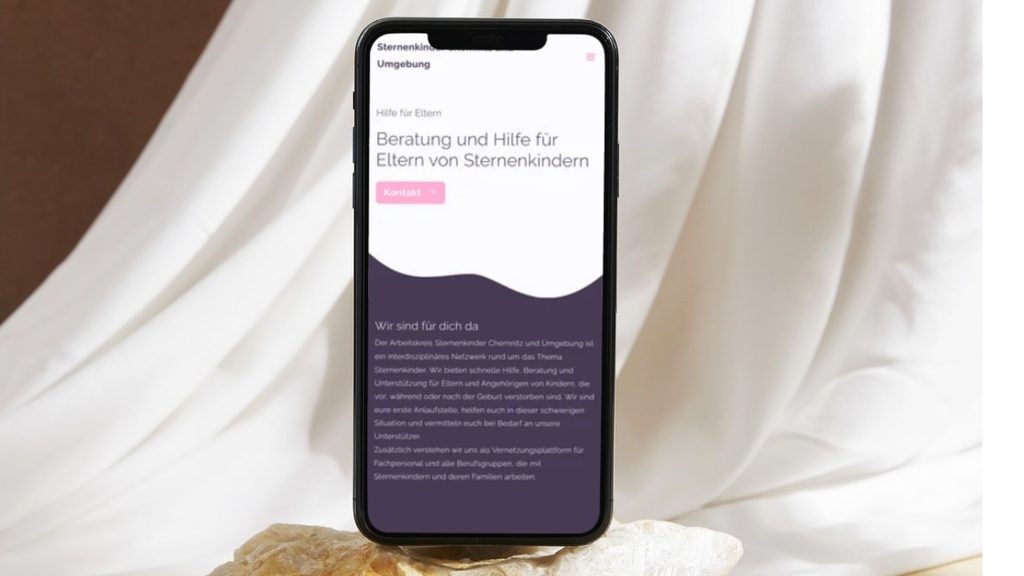 Smartphone steht auf einem beigen Sofa. Geöffnet darauf ist das neue umgesetzte WordPress Webdesign von melaniemueller.design für sternenkinder-chemnitz.de