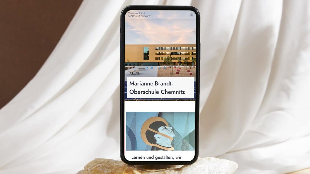 smartphone auf beigen Grund mit WordPress Redesign der marianne brandt oberschule chemnitz von melaniemuellerdesign
